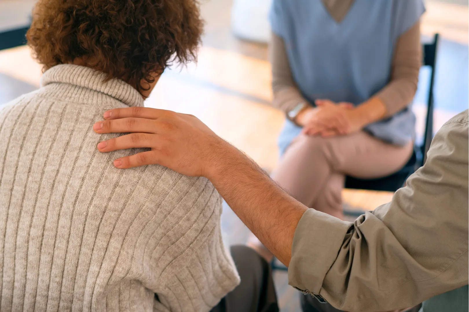 A hand on a shoulder offers comfort during an Abuse Counseling & Therapy support group session.