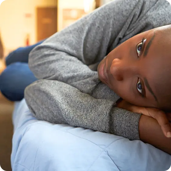 A thoughtful person rests on a bed, illustrating the trauma-informed care at Abuse Counseling & Therapy.