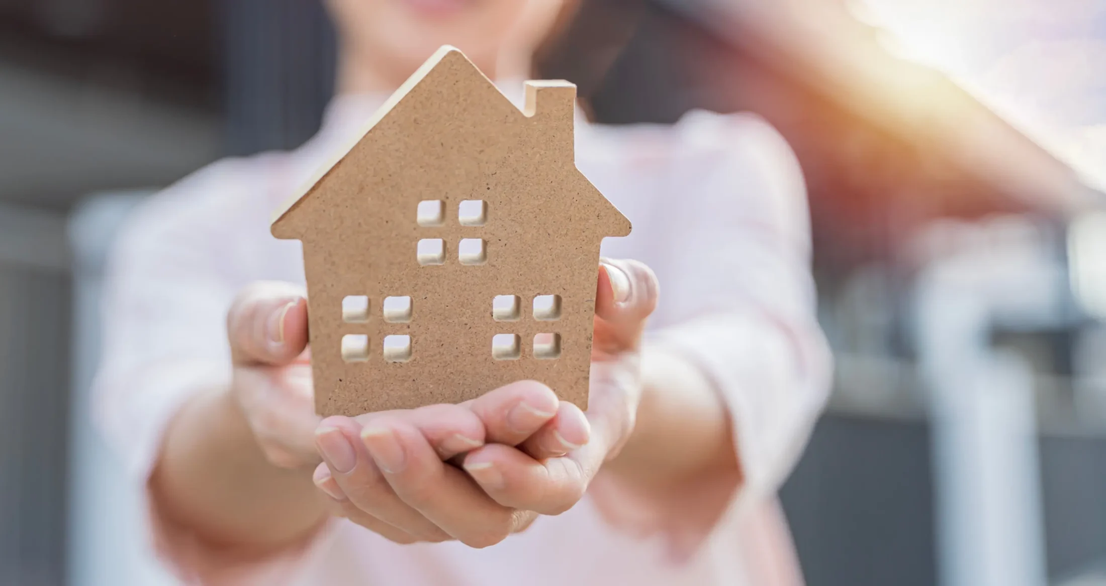 Hands hold a wooden house model, representing safe shelter provided by Abuse Counseling & Therapy.