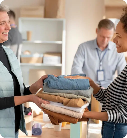 A volunteer at Abuse Counseling & Therapy hands a stack of folded clothes to a smiling woman.