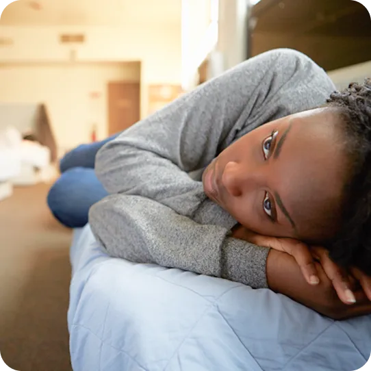 A pensive woman rests on a cot at an Abuse Counseling & Therapy shelter.