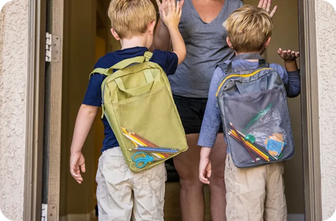 Two boys with backpacks wave goodbye to a mother, representing Abuse Counseling & Therapy's family care.