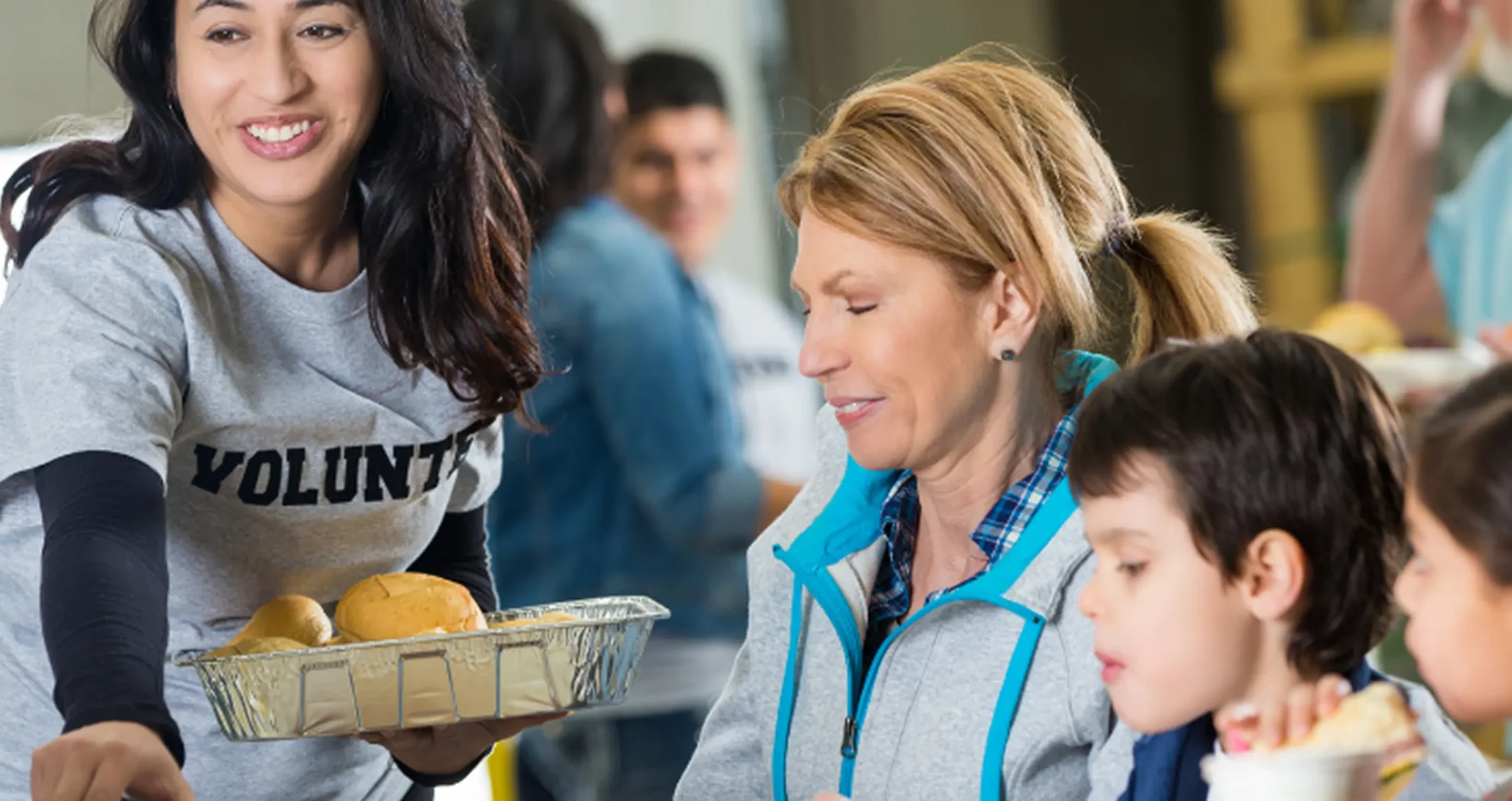 An Abuse Counseling & Therapy volunteer serves food to a smiling mother and her children.