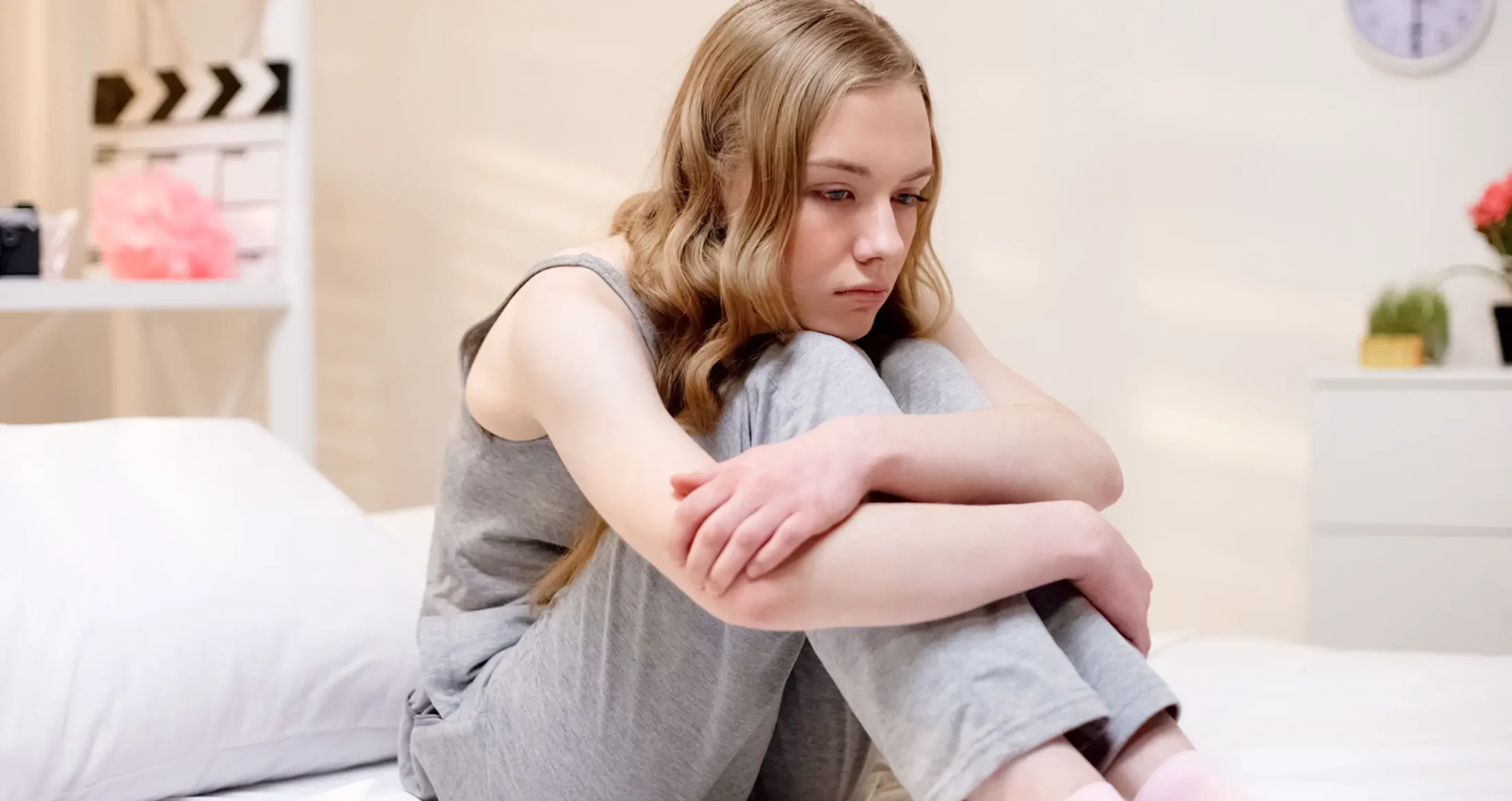 A sad young woman sits on a bed hugging her knees, a survivor supported by Abuse Counseling & Therapy.