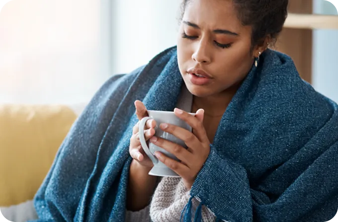 A distressed woman wrapped in a blanket holds a warm mug, seeking help from Abuse Counseling & Therapy.