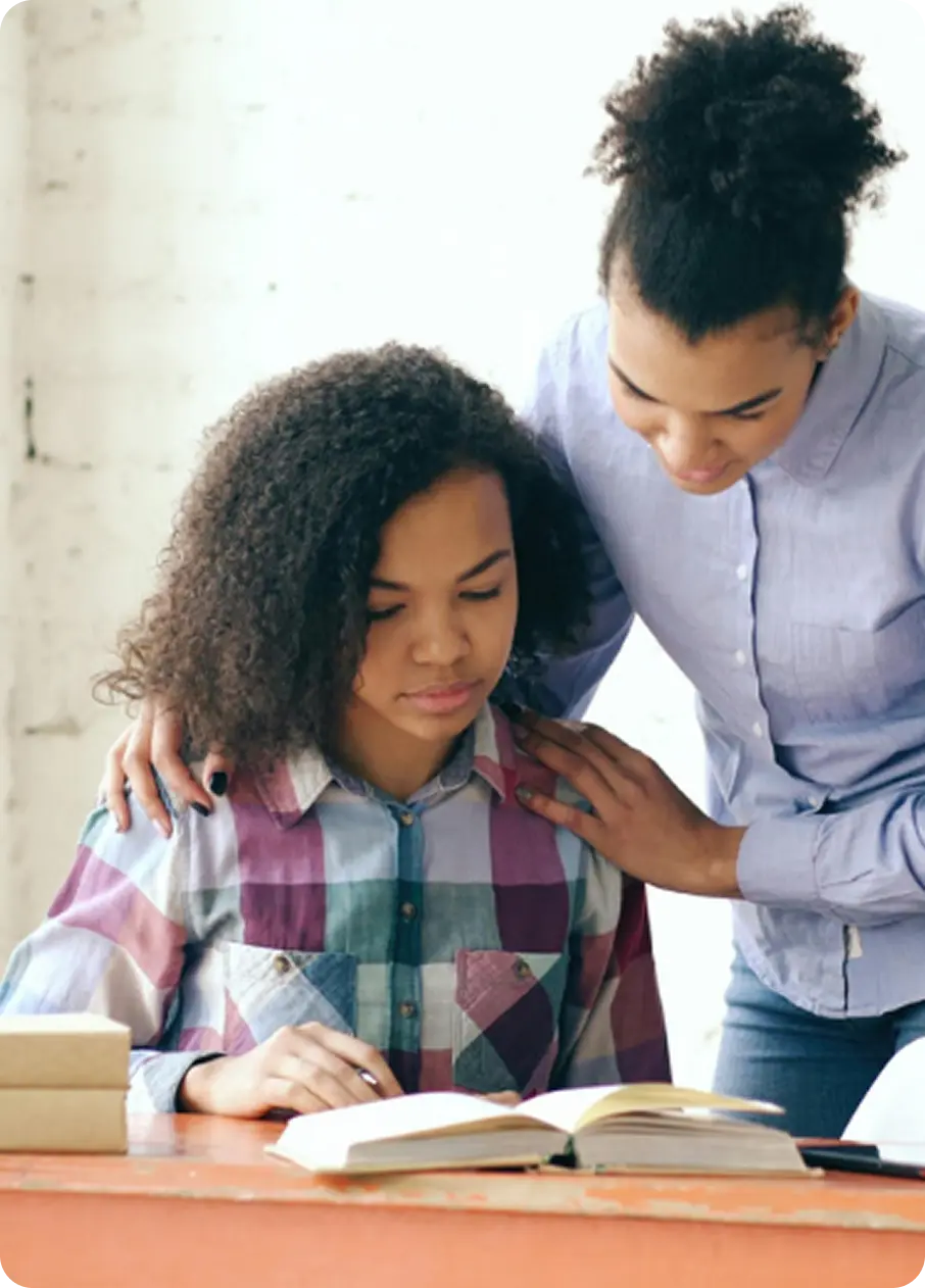 An Abuse Counseling & Therapy therapist offers gentle support to a young girl studying at a desk.