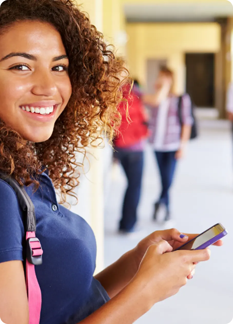 A smiling student uses her phone to access Abuse Counseling & Therapy services in a school hallway.