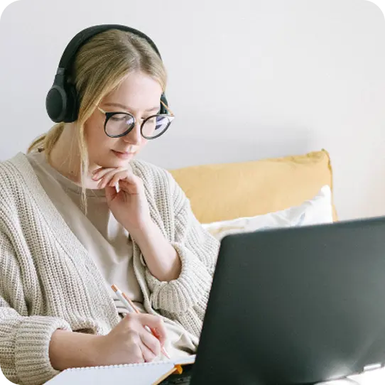 A woman wearing headphones takes notes during an online session with Abuse Counseling & Therapy.