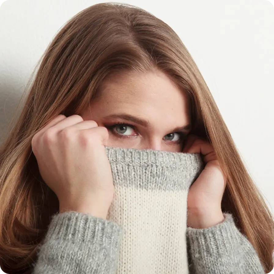 A woman covering her face with a sweater, representing survivors supported by Abuse Counseling & Therapy.