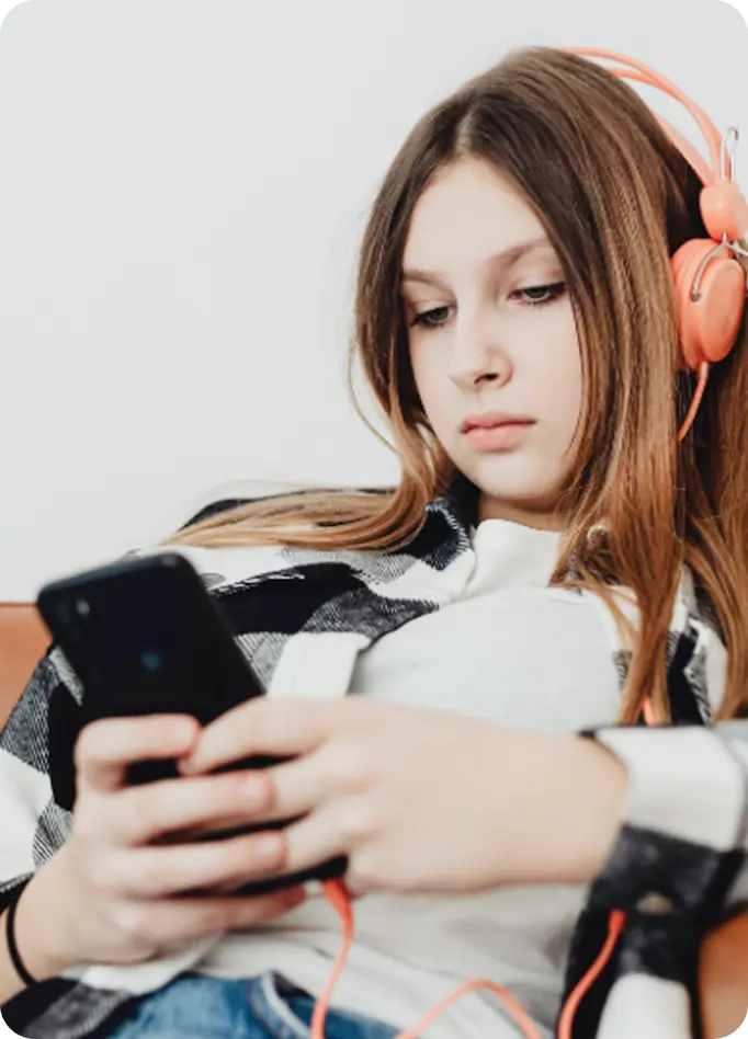 A young woman wearing headphones uses her phone to access Abuse Counseling & Therapy support.