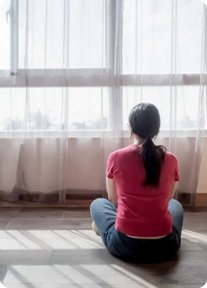 A woman sits peacefully facing a bright window, supported by Abuse Counseling & Therapy.