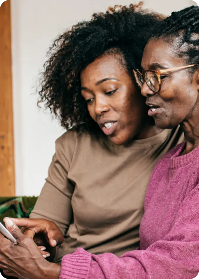 Two Black women of different ages look at a phone during an Abuse Counseling & Therapy support session.