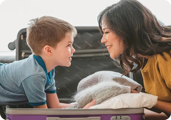 A smiling mother and son pack a suitcase, finding a safe new beginning with Abuse Counseling & Therapy.