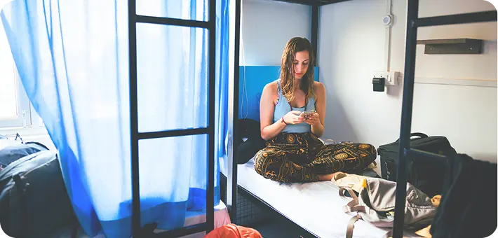 A woman sits on a bunk bed using her phone inside an Abuse Counseling & Therapy shelter.