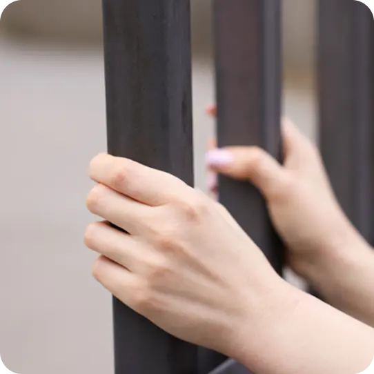 A person's hands grip dark metal bars, symbolizing the trauma support from Abuse Counseling & Therapy.